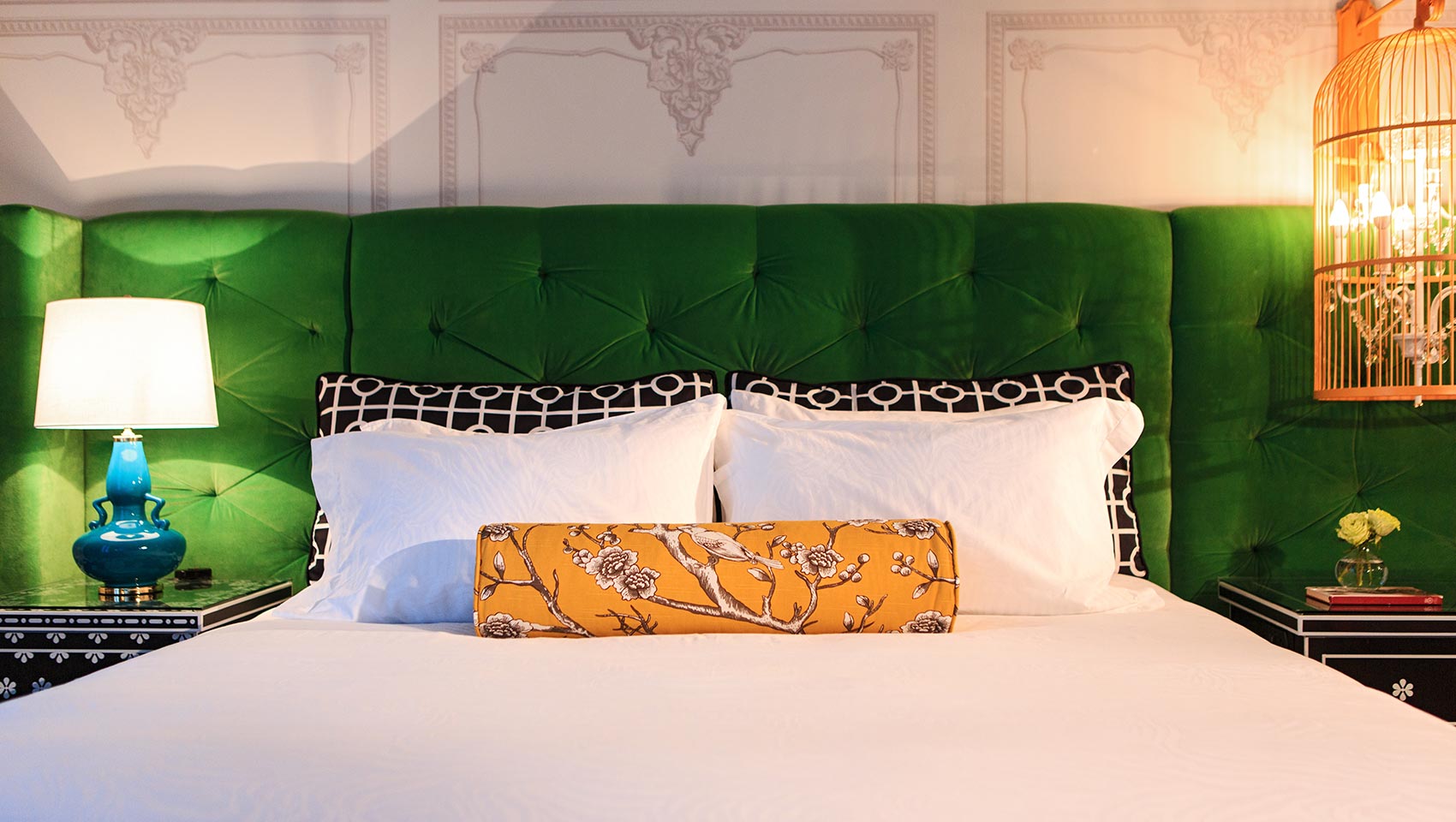 a hotel room bed with a green headboard and yellow throw pillow